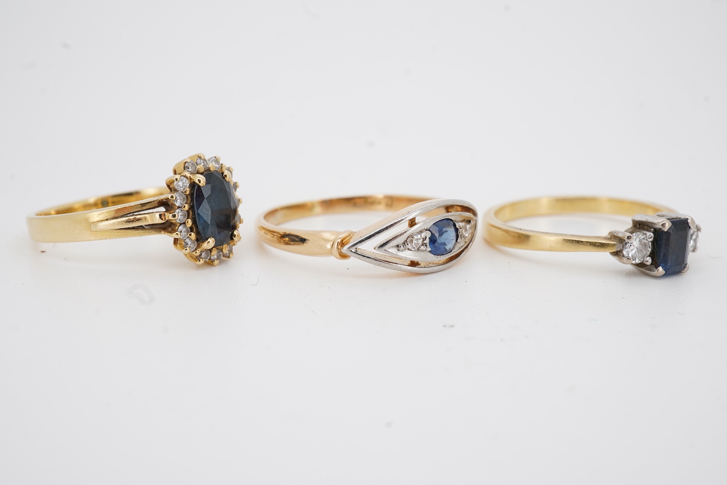 A modern 18ct gold, single stone sapphire and two stone diamond set ring, size O, an 18k, sapphire and diamond set oval cluster ring, size M/N and an 18ct, single stone sapphire and two stone diamond chip set navette sha
